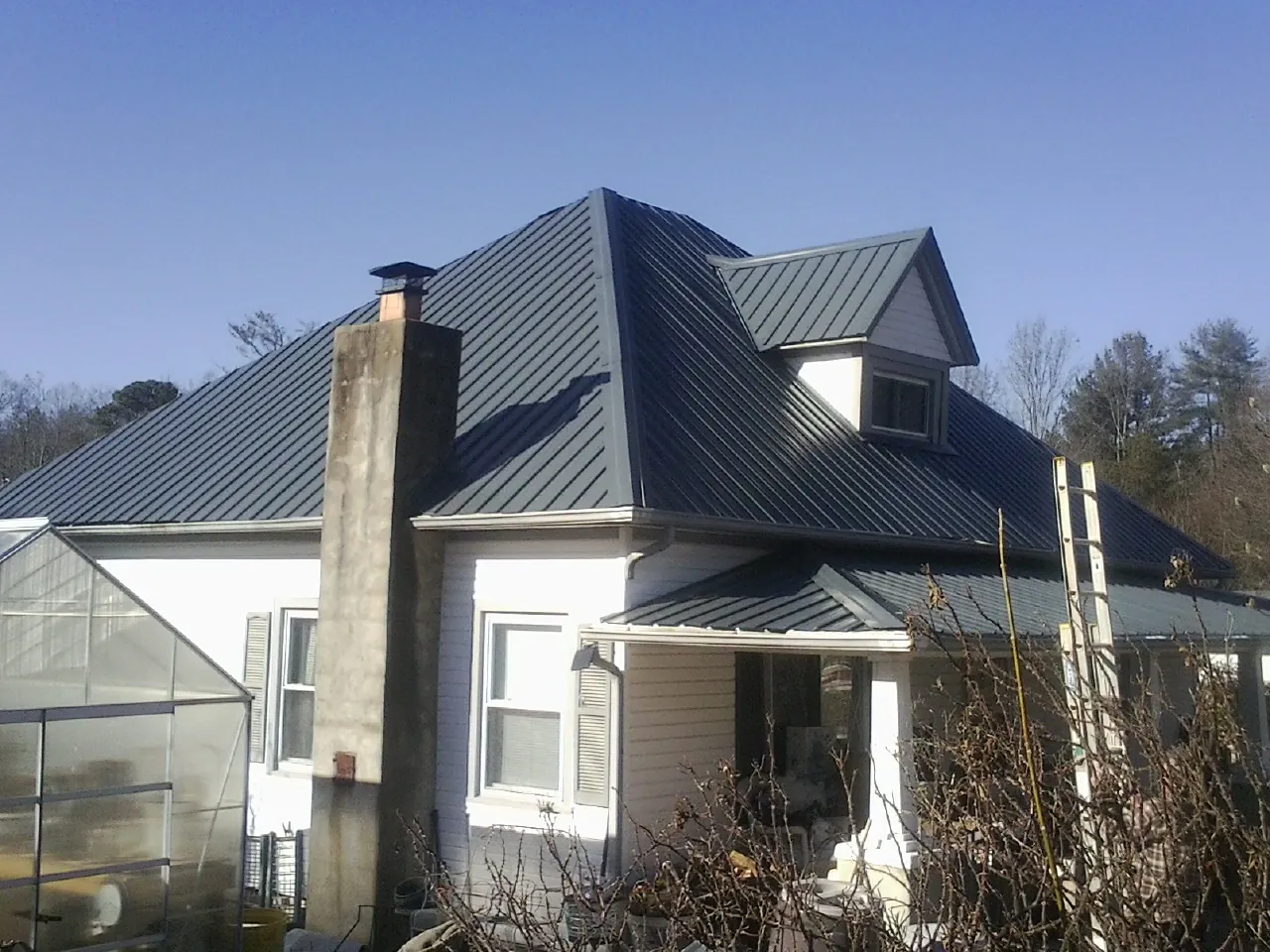 Dark blue standing seam metal roof on a white farmhouse with dormer — Slate & Tile Roof Repair by Roofing Brothers in Martensdale