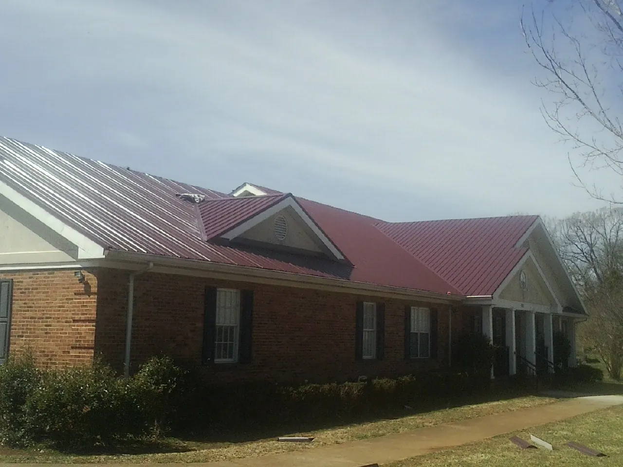 Red metal roof with gabled entries on a long brick building, from a Hail Damage Roof Repair job in Martensdale