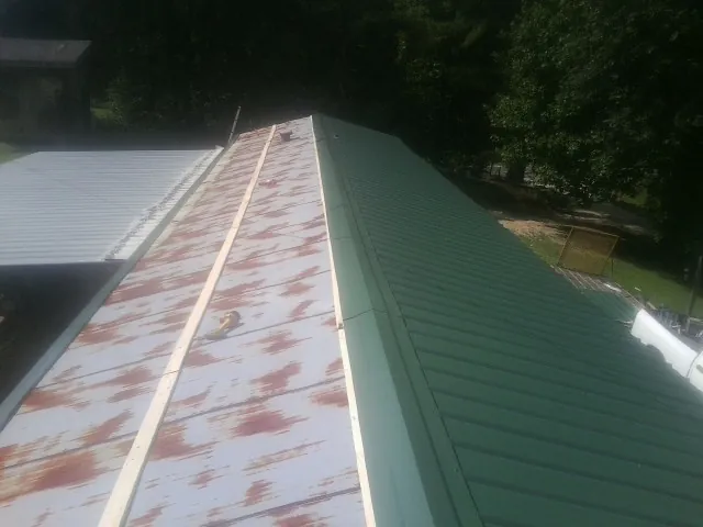 Old rusted panels beside newly installed green metal roofing — Wind Damage Roof Repair by Roofing Brothers in Martensdale