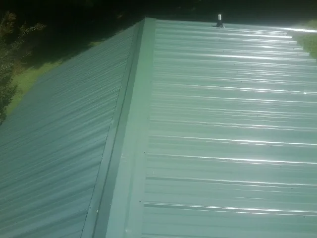 New green metal panels meeting at the ridge of a roof — Flat Roof Repair work by our crew in Martensdale