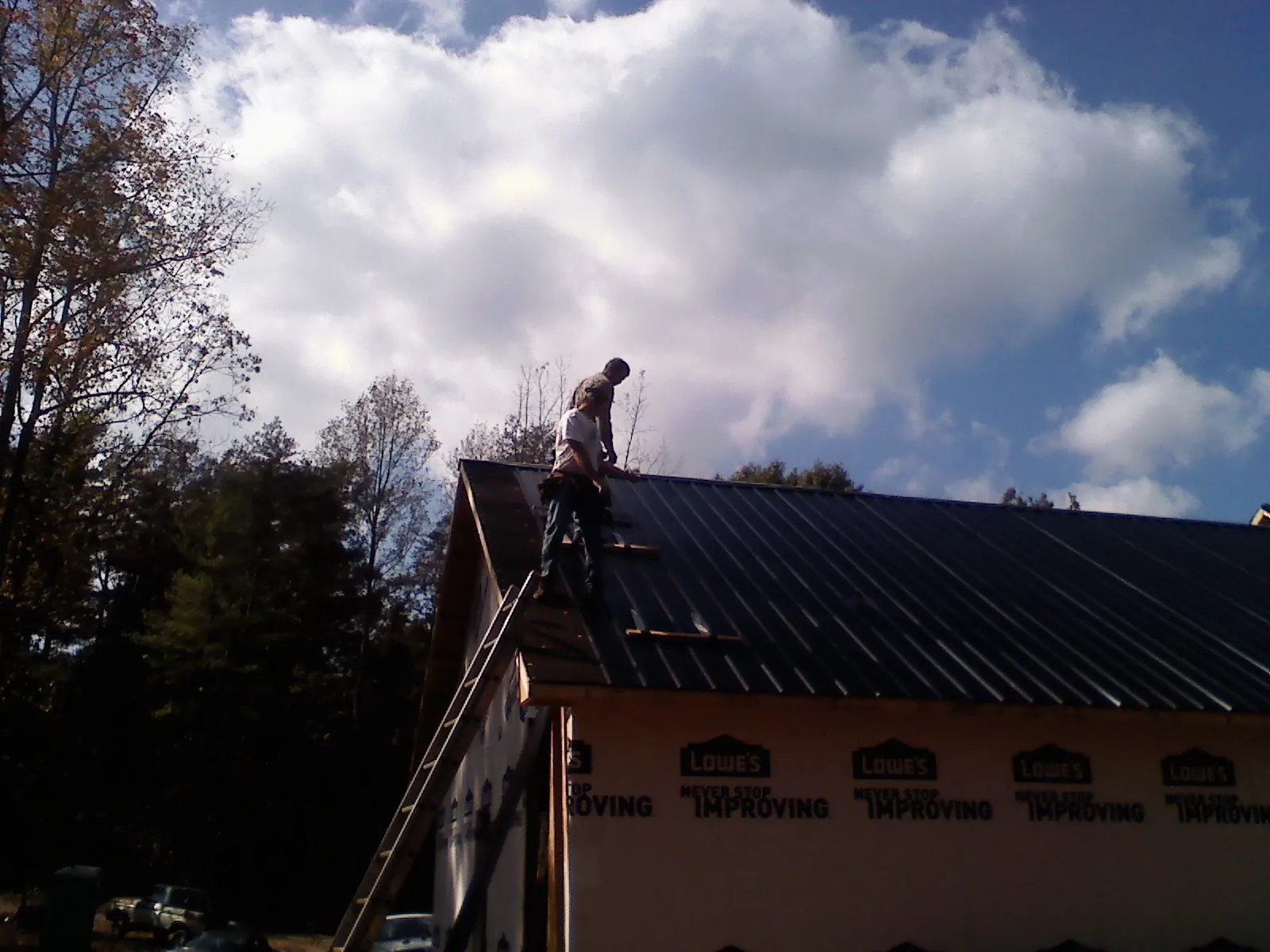 Roofer fastening dark metal panels high against a cloudy sky, from a Roof Inspection job in Martensdale
