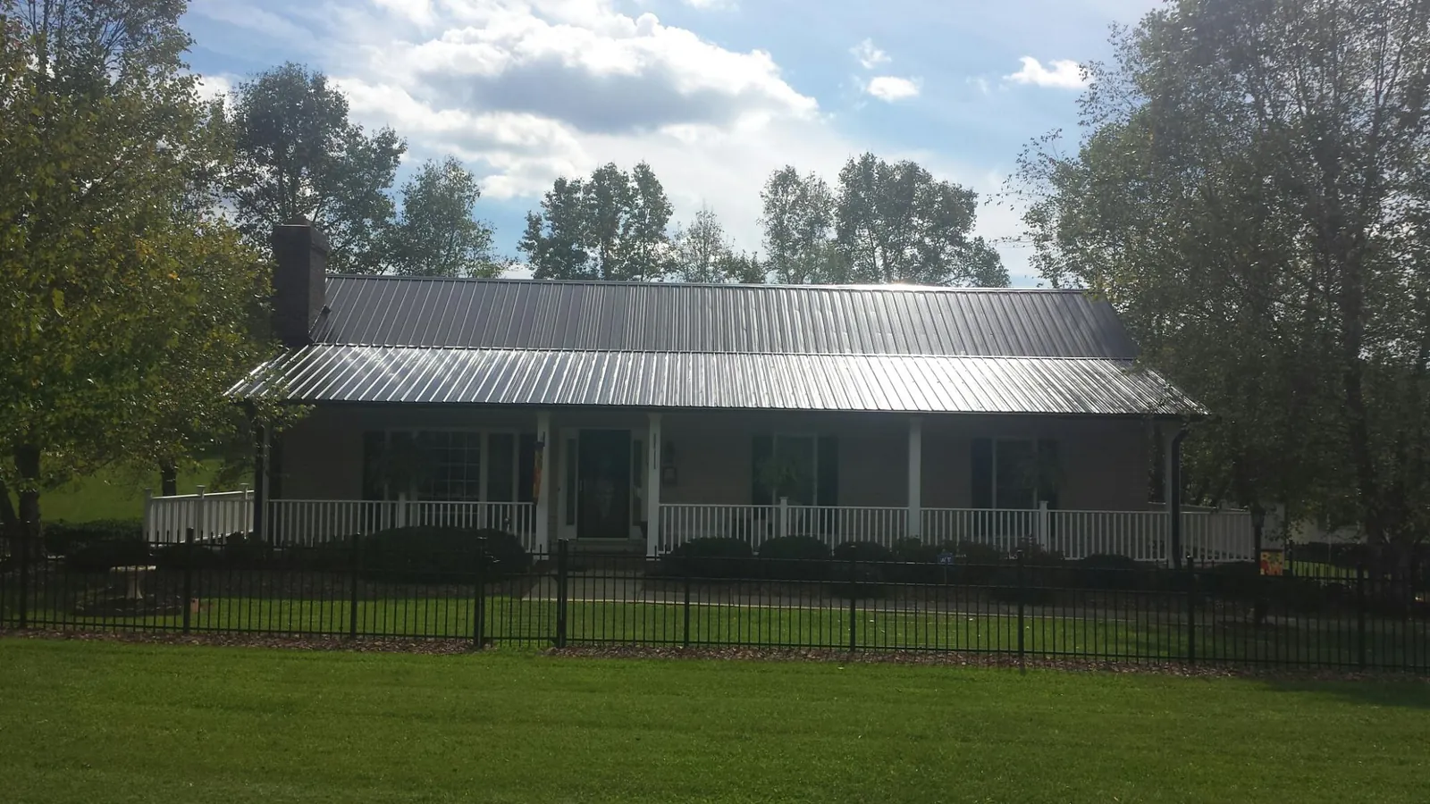 Gray metal roof on a brick ranch with a full width front porch — Gutter Guard Installation work by our crew in Martensdale