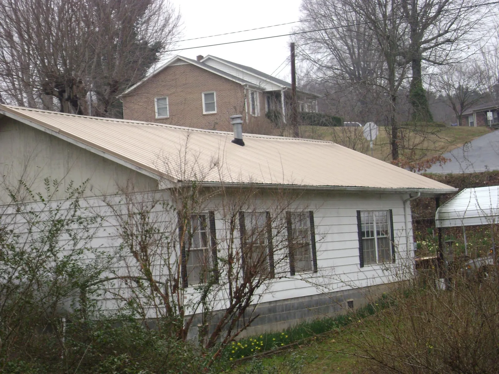 Tan metal roof on a white sided house set into a hillside — Commercial Roofing by Roofing Brothers in Martensdale