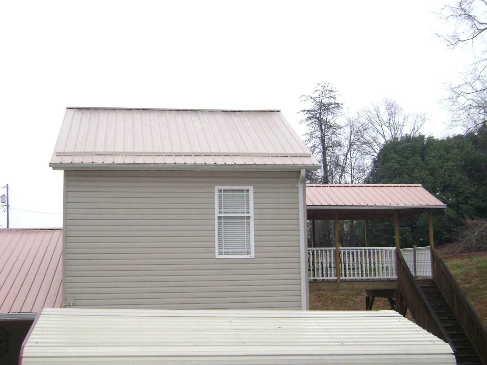 Tan metal roofs on a two story addition and attached porch, from a Roof Replacement job in Martensdale